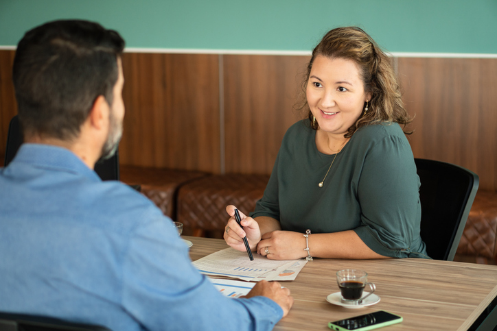 A recruiter and candidate in an engaged face-to-face conversation at a café table, with documents between them